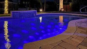 Ein Schwimmbecken mit beleuchteten Palmen und einer gefliesten Kante.