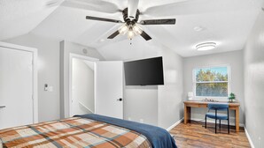 A bedroom with a bed, ceiling fan, TV, desk, chair, window, and wooden flooring. - Newly Remodeled Condo in the Heart of Springfield (Springfield)