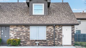 A residential building with a brick facade, a dormer window, a garage door, and a small garden area. - Newly Remodeled Condo in the Heart of Springfield (Springfield)