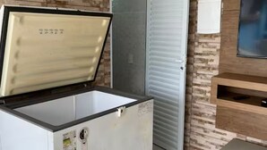 A compact refrigerator with a freezer compartment, a wooden shelf unit, and a sliding door closet.
