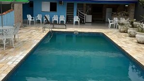 A rectangular pool with a tiled deck, surrounded by white plastic chairs and potted plants.