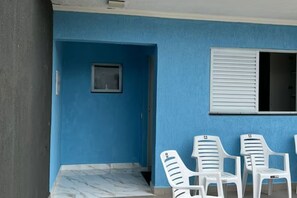 Eine blaue Außenwand, ein kleines Fenster und drei weiße Plastikstühle.
