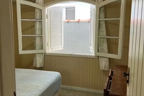 Ein Schlafzimmer mit einem Bett, einem Fenster mit Rollläden und einem Holzschrank.