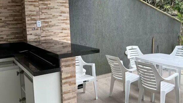 An outdoor kitchen area with a black countertop, white cabinets, and a table with white plastic chairs.