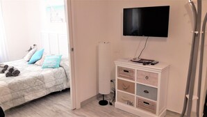 Et soveværelse med en seng, et fjernsyn ophængt på væggen, en radiator og et opbevaringsskab med skuffer.