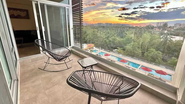 Ein Balkon mit zwei Stühlen, einem kleinen Tisch und Blick auf eine Stadtlandschaft bei Sonnenuntergang.