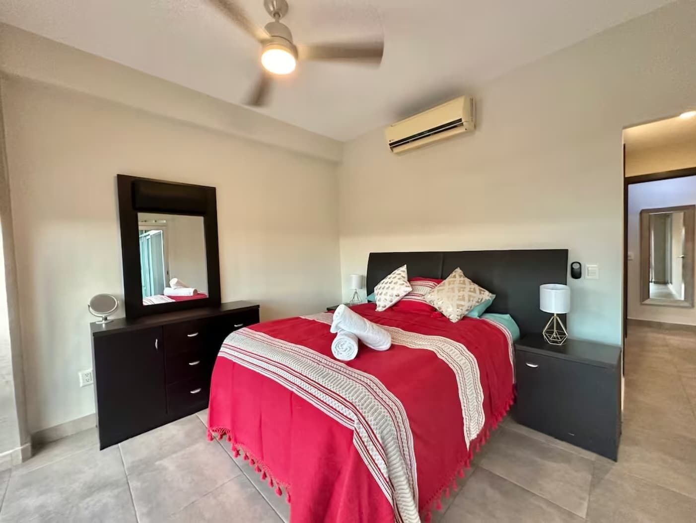 A bedroom with a bed, a dresser, a mirror, an air conditioner, and a ceiling fan.