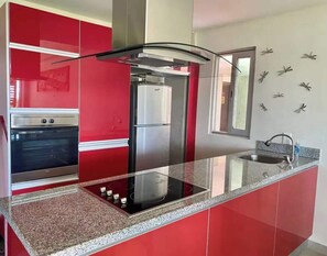 Eine moderne Küche mit roten Schränken, einem eingebauten Ofen, einem Edelstahlkühlschrank und einer Granit Arbeitsplatte.