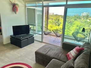 Ein modernes Wohnzimmer mit Flachbildfernseher, einer Couch und einem Balkon mit Sitzgelegenheiten.