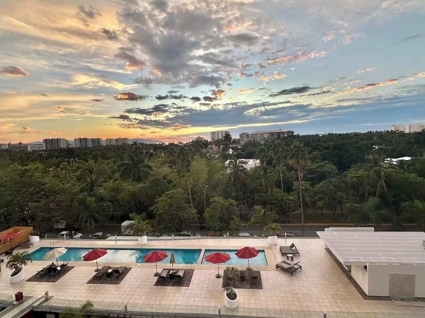 A rooftop pool area with multiple pools, lounge chairs, and umbrellas.