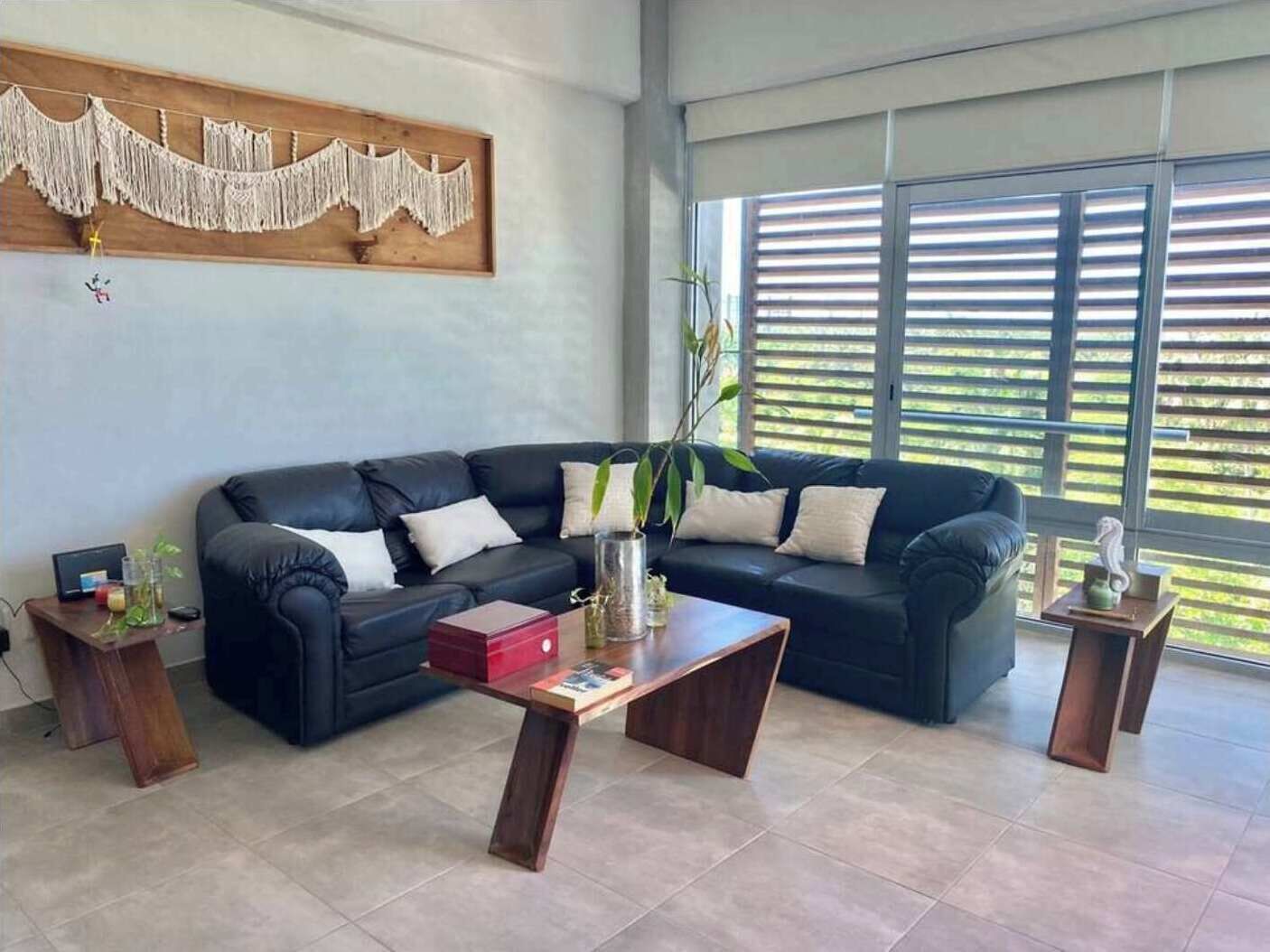 Un soggiorno con un divano in pelle nera, un tavolino in legno e un arazzo macramè.