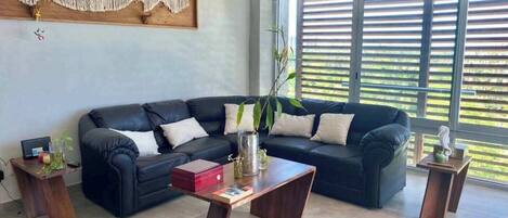 A living room with a black leather sofa, wooden coffee table, and a macrame wall hanging.