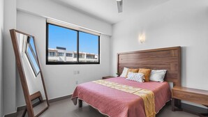 Ein Schlafzimmer mit großem Fenster, einem Bett mit Holz Kopfteil, einem Nachttisch und einem Spiegel.