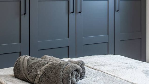 Een slaapkamer met een bed, een grijze garderobe en een opgerolde handdoek op het bed.
