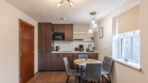 Een kleine keuken met houten kastjes, een ingebouwde magnetron en een eethoek met een ronde tafel en vier stoelen.
