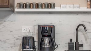 Een moderne keuken met een Bosch koffiezetapparaat, een marmeren aanrecht, een spoelbak en een plank met wijnglazen en koffiemokken.