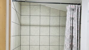 Un baño con ducha, paredes de azulejos y bañera.