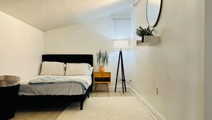 Un dormitorio con cama, mesita de noche, lámpara y una pequeña estantería.