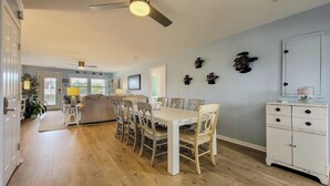 A spacious living area with a dining table, chairs, a ceiling fan, and a kitchen area with cabinets. - Tide Dyed – A Colorful Coastal Escape (Topsail Beach)
