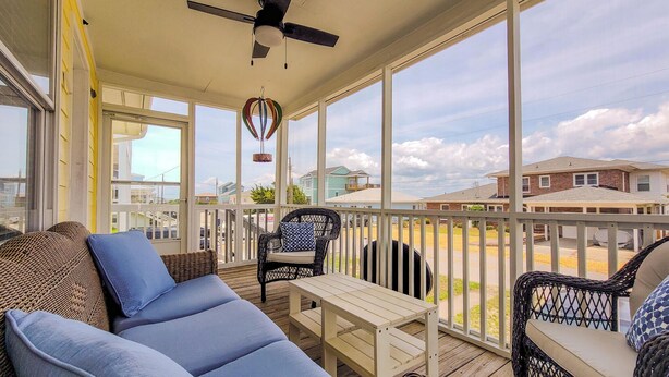 A covered outdoor area with a ceiling fan, wicker furniture, and a view of neighboring houses. - Tide Dyed – A Colorful Coastal Escape (Topsail Beach)