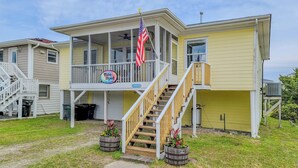 A two-story house with a porch, a staircase, and an American flag. - Tide Dyed – A Colorful Coastal Escape (Topsail Beach)