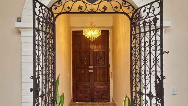 A hallway with a patterned floor, a wooden door, and a decorative metal gate. - Hotel Casa Dharma (Popayán)