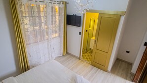 A bedroom with a bed, curtains, a chandelier, a TV, and a door leading to another room. - Hotel Casa Dharma (Popayán)