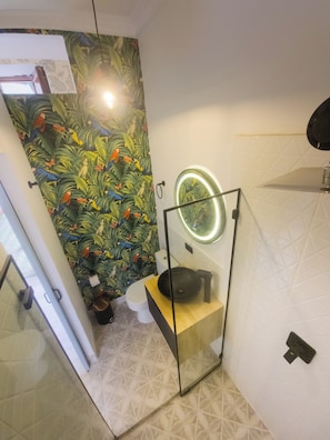 Un baño de diseño moderno, con inodoro, lavamanos con recipiente, espejo con luz y pared con estampado.