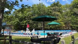 A pool area with lounge chairs and umbrellas, surrounded by trees.