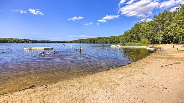 A lake with clear water, a sandy beach, and trees in the background.