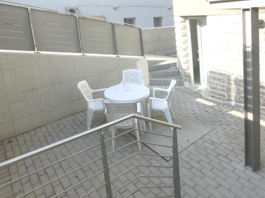 Un patio con una mesa redonda y cuatro sillas, baranda de metal y piso de ladrillo.