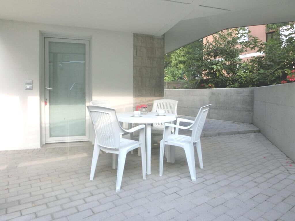 A patio with a table and chairs, a door, and a view of greenery.