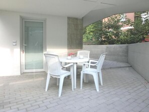 A patio with a table and chairs, a door, and a view of greenery. - Modern Residence Just Steps From the Beach (Lignano Sabbiadoro)