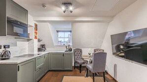 Angolo cottura compatto con forno a microonde, bollitore e macchina da caffè, zona pranzo con tavolo e sedie, e TV fissata al muro.