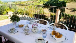 Una mesa dispuesta para un servicio de té, con tazas, platitos y una tetera, rodeada de sillas de mimbre.