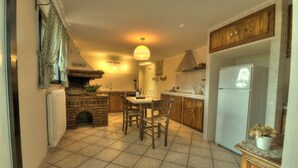 Una cocina con chimenea, armarios de madera, una mesa de comedor con sillas y un refrigerador.