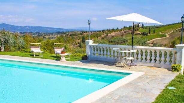 Una piscina con borde de piedra, rodeada por una balaustrada blanca, con vistas a un paisaje pintoresco.