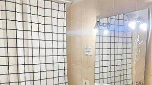 Une salle de bain avec un rideau de douche à motifs géométriques, un lavabo blanc avec un miroir au-dessus, et un porte-serviettes avec des serviettes pliées.
