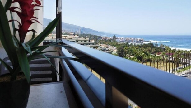 Un balcon offrant une vue sur un paysage urbain côtier, avec des bâtiments et une plage.