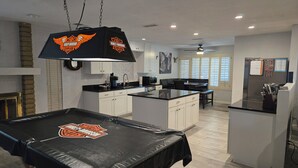 Une cuisine moderne avec des meubles blancs, un plan de travail noir et une table de billard ornée du logo Harley-Davidson.