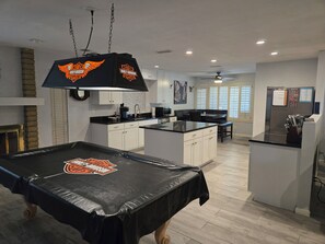 Eine moderne Küche mit weißen Schränken, einer schwarzen Arbeitsplatte und einem Billardtisch mit Harley-Davidson-Logo.