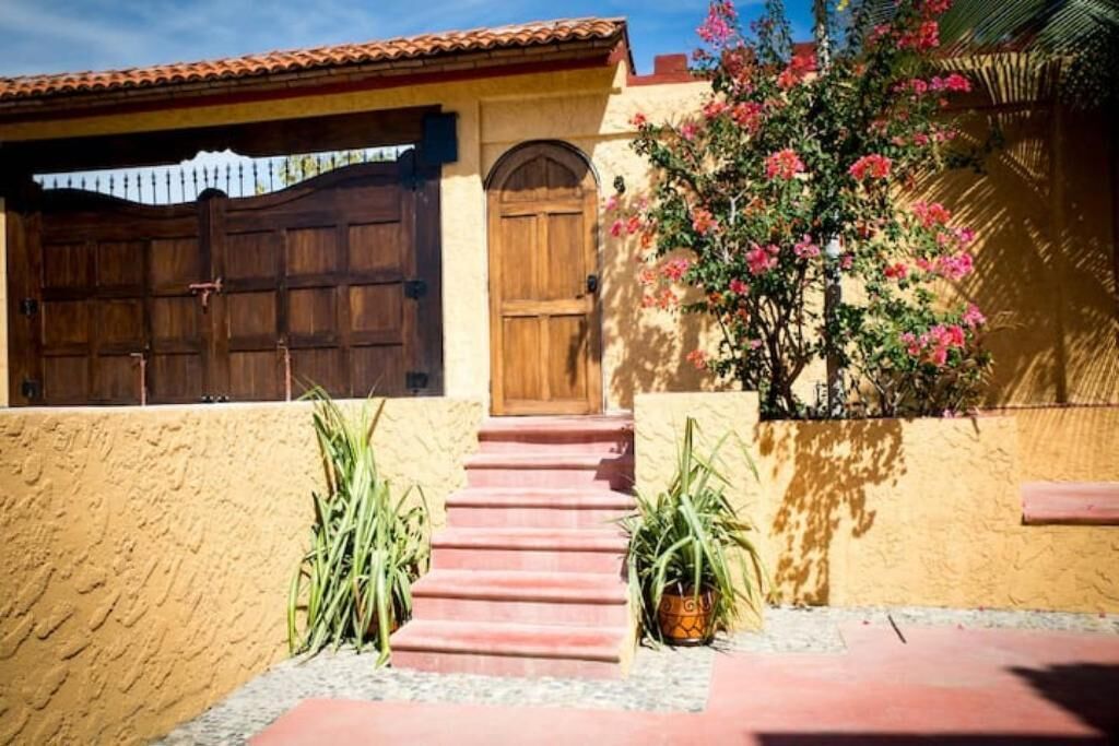 Un bâtiment avec une porte en bois, un escalier menant à l’entrée et une plante en fleurs.
