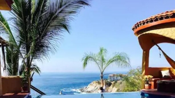 A pool with a view of the ocean, palm trees, and a building with a curved roof. - Villa Xcaanda (San Pedro Pochutla)