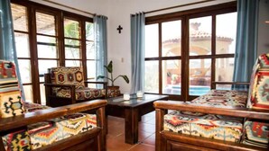A room with large windows, wooden furniture, and a view of a pool. - Villa Xcaanda (San Pedro Pochutla)