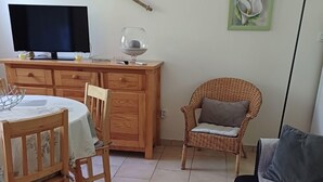 A room with a dining table, chairs, a sofa, a television, a decorative wall piece, and a floor lamp.