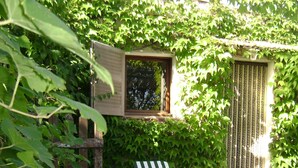 A patio area with white plastic chairs and a table, surrounded by lush greenery.