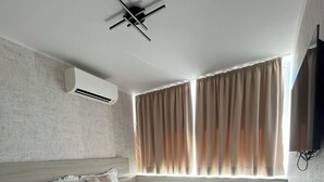 A modern hotel room with a bed, air conditioning unit, curtains, and a ceiling fan.