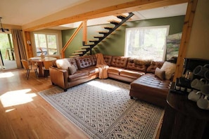 Ein geräumiges Wohnzimmer mit einer Holztreppe, einem Ecksofa, einem Esstisch und einem gemusterten Teppich.