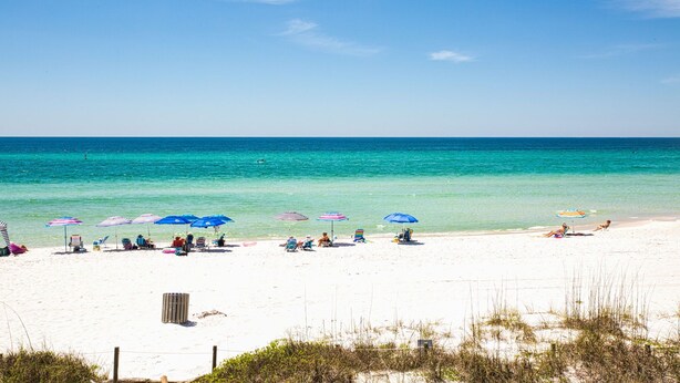 Une plage de sable blanc, avec une eau turquoise et limpide, et plusieurs parasols de plage.
