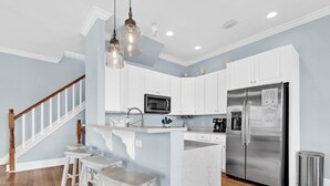 Une cuisine moderne avec des meubles blancs, un réfrigérateur en acier inoxydable, un four à micro-ondes encastré et un escalier en bois.
